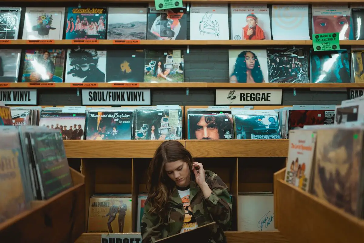 Image of a person in a record store with vinyl records categorized based on music genre. Source: unsplash