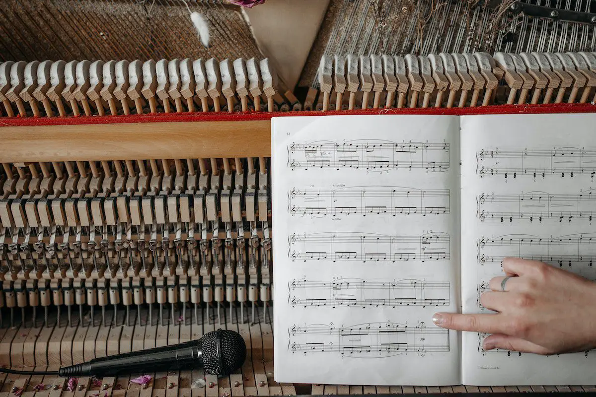 Image of a person pointing at a music sheet on top of a piano. Source: pexels