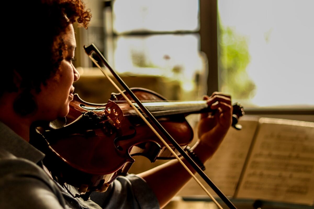 Image of a violinist playing the violin while looking at sheet music. Source: unsplash