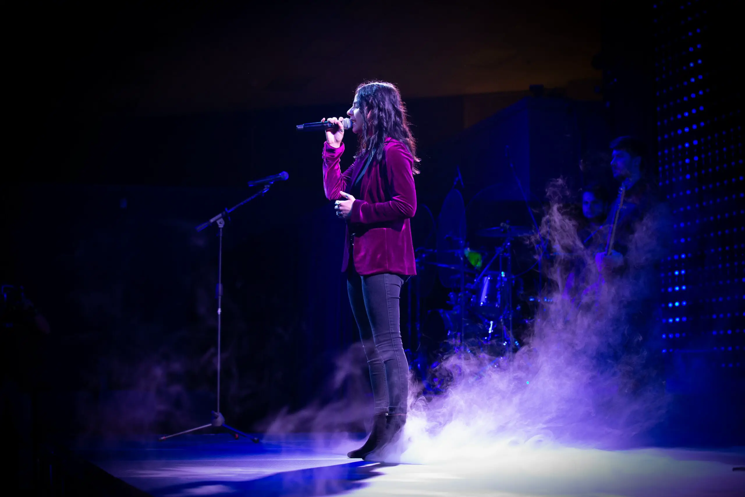 Image of a female singer wearing a maroon sweater, black jeans, and black boots.