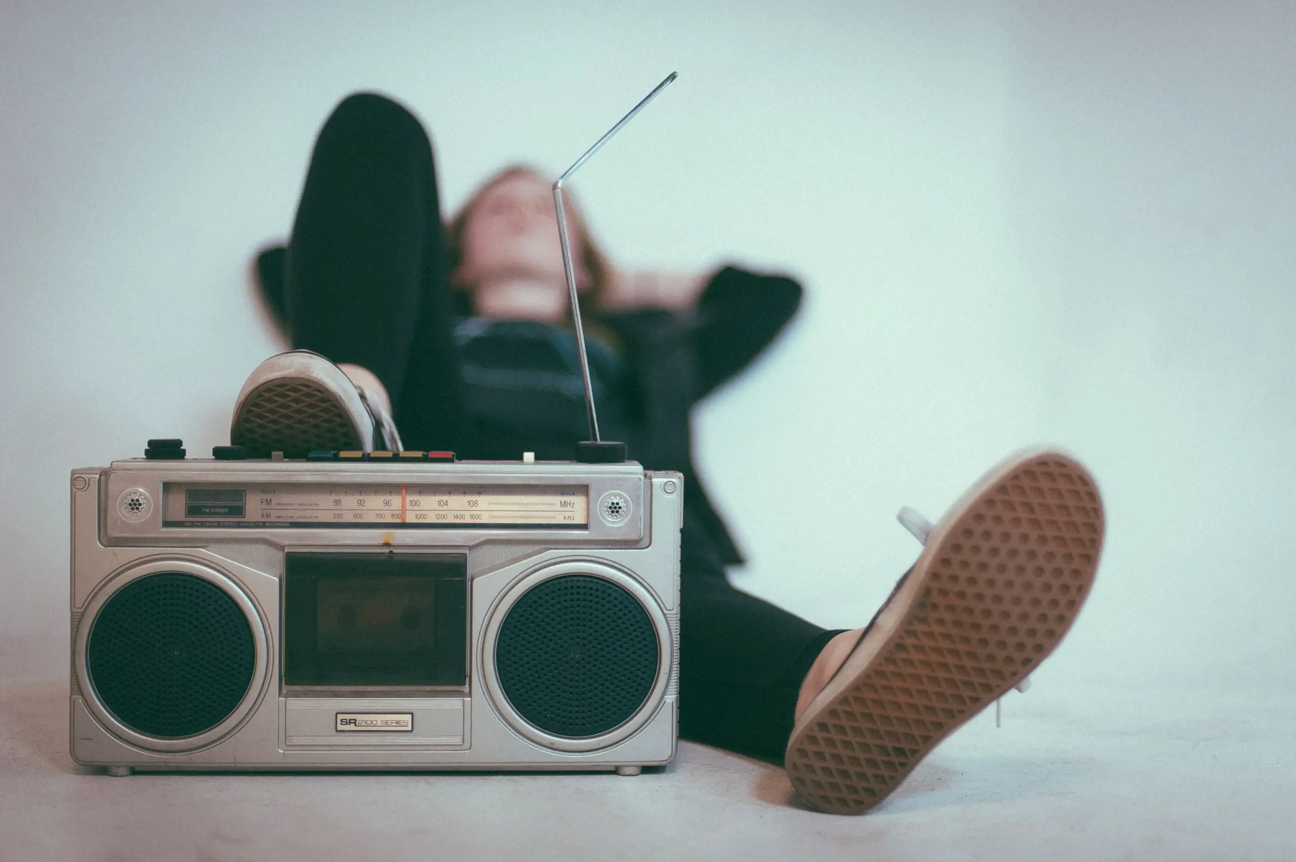 Image of a man lying on the floor while listening to songs in a cassette radio.