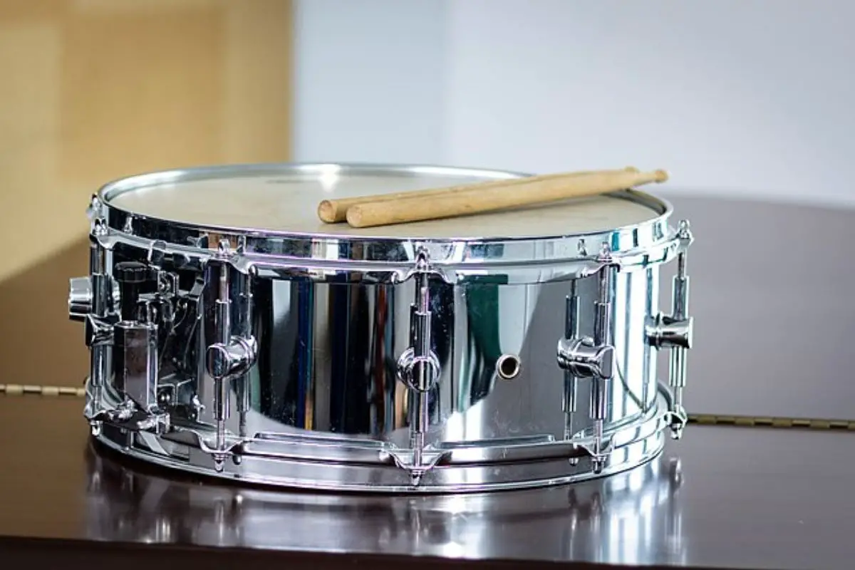 Image of a metal snare drum with two drumsticks on top.
