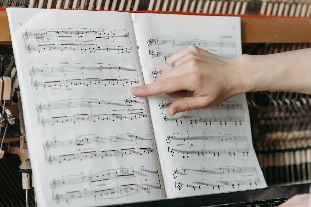 Image of a person pointing at a note in sheet music. Source: pexels
